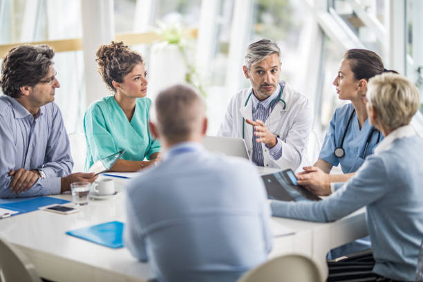 Male doctor and his female colleagues talking to team of business people on a meeting in the hospital.